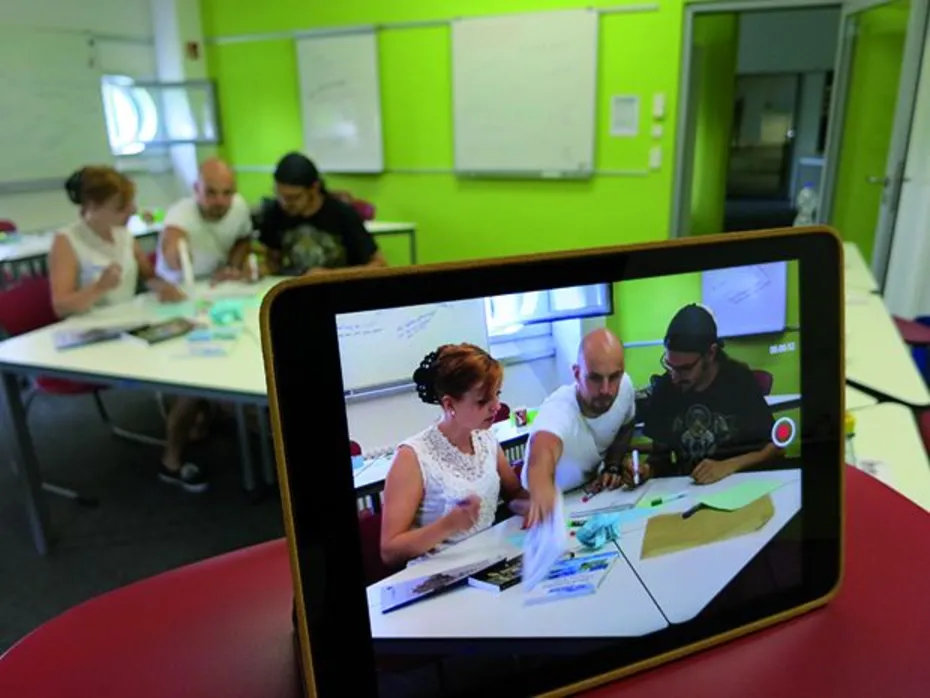 Foto zeigt drei Personen an einem Tisch über einen Tabletbildschirm Foto zeigt drei Personen an einem Tisch über einen Tabletbildschirm